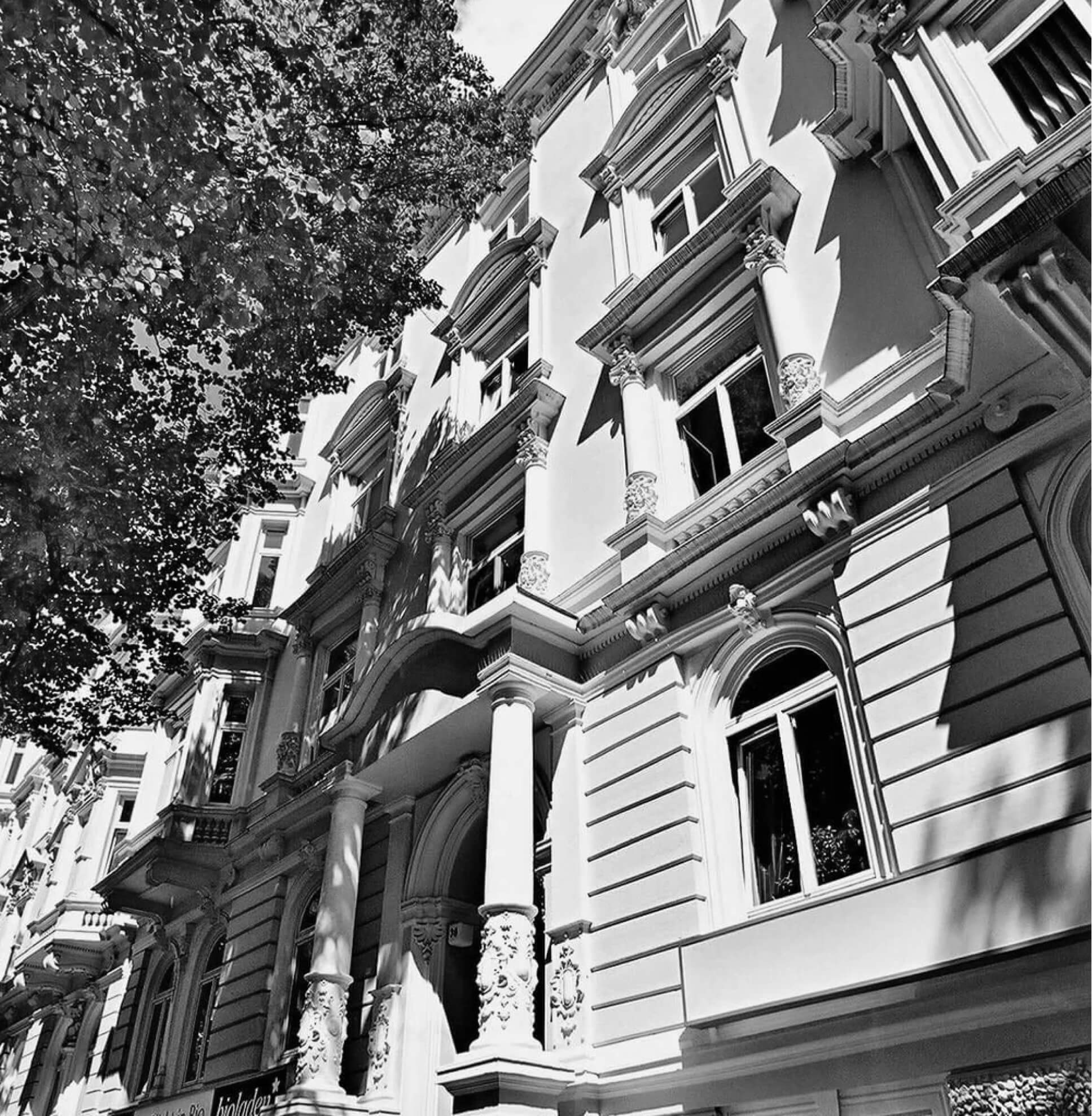 Historische Fassade mit dekorativen Säulen und Fenstern, Schwarz-Weiß-Aufnahme, von unten betrachtet.